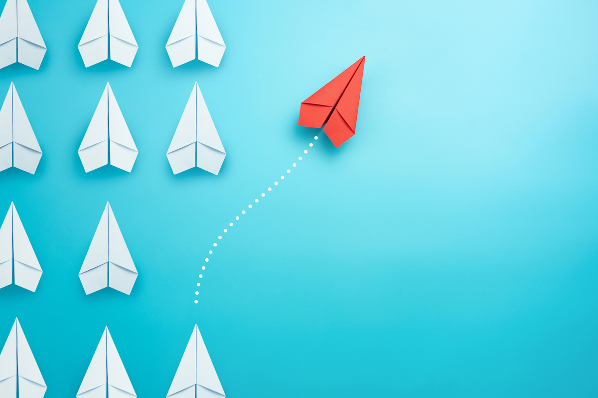 Group of white paper plane in one direction and one red paper plane pointing in different way on blue background. Business for innovative solution concept.